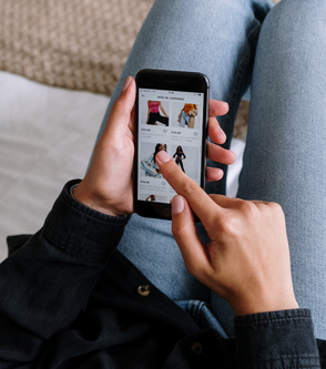 a woman holding a cell phone with a shopping app on it.